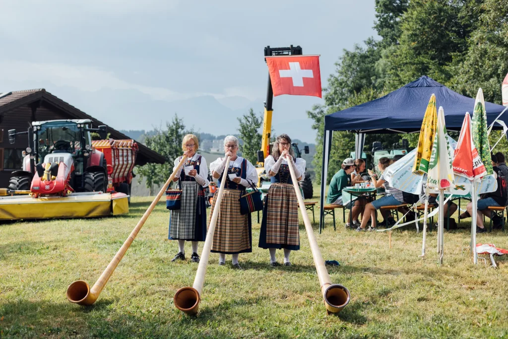Donne in costume tradizionale suonano il corno delle Alpi sul prato della festa.
